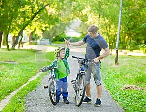 Father and son give high five while cycling in the park