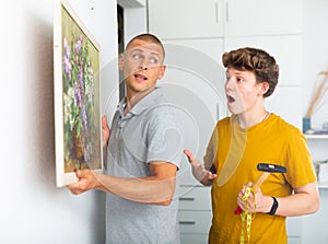 Father and son hang picture together on the wall of house