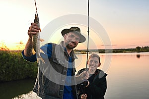 The first joint fishing of adult father and teen son in warm, sunny day.