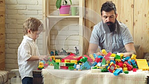 Father and son with happy faces create colorful constructions with toy bricks. The boy and his father play with the