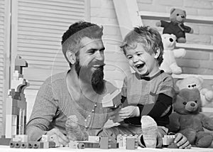 Father and son with happy faces create colorful toy gun with bricks. Boy and man play together. Dad and kid with toys