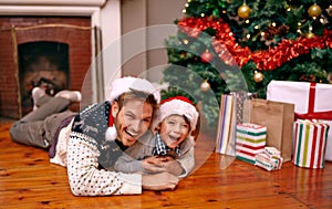 Father, son and happy with portrait on christmas for celebration, playing and love on floor with santa hats. Family, man