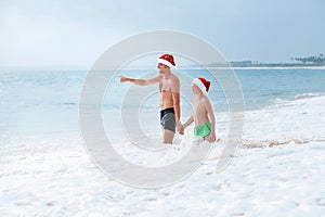 Father and son have a fun on ocean beach, wait a big waves. Christmas holiday time. Tropical vacation