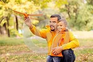 Father and son having fun in autumn park, launching toy airplane outdoors. Yellow trees in background