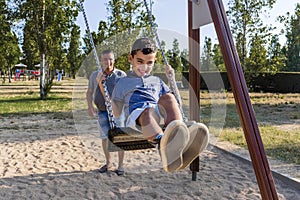 Father and son having fun playing with the swing in a park.