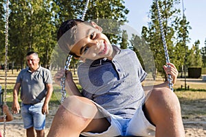 Father and son having fun playing with the swing in a park.