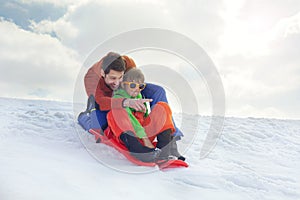 Father and son having fun in the snow, sliding