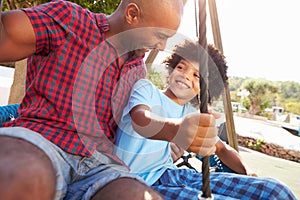 Father And Son Having Fun On Swing In Playground