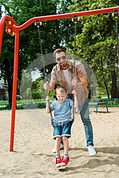 father and son having fun on swing at playground in park and looking