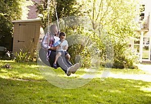 Father And Son Having Fun On Tire Swing In Garden