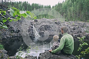 Father and son hikers travellers sitting near mountain waterfall. Peaceful and calmness scenic view. Active family outdoors photo