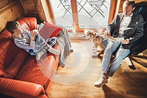 Father, son and his beagle dog spending holiday time in cozy country house. Dad reading a book, boy sitting and listening, dog