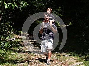 Father with son on his shoulders comes down from a forest path o