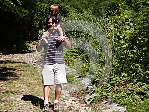Father with son on his shoulders comes down from a forest path o