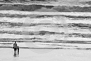 Father and son holding hands on the beach at the pacific ocean at sunset with waves