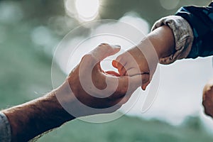 Father and son holding hands outdoors close-up, cute strong dad holding child`s arm, parenting and trust concept