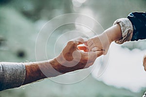 Father and son holding hands outdoors close-up, cute strong dad holding child`s arm, parenting and trust concept