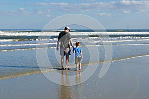 Father and son holding hands while walking on the beach