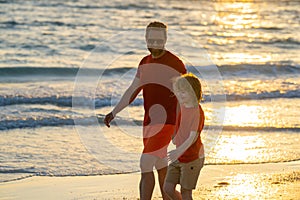 Father and son holding hands walking on sunset beach. Father and son walk in sea beach. Concept of friendly family