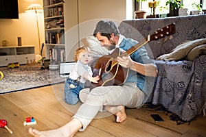 Father and son at home playing guitar together.