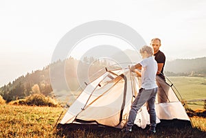 Father and son installing tent on forest glade.Trekking with kids concept image