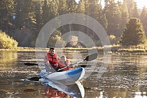 Father and son kayaking on rural lake, front view