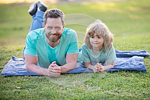 Father and son laying on grass in park. People having fun outdoors. Concept of happy vacation and friendly family.