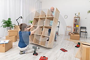 A father and son lift a folding bookcase upright.