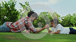 Father and son lying on grass in field. Boy and man competing in arm wrestling