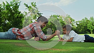 Father and son lying on grass in field. Boy and man competing in arm wrestling