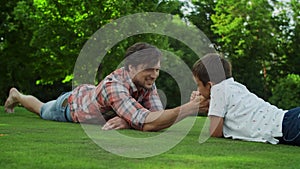 Father and son lying on grass in field. Man and boy competing in arm wrestling