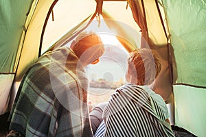 Father and son meet a sunset in mountain, look out from tent