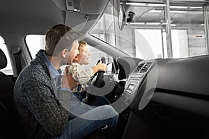 Father and son observing new car cabin in dealership.