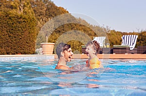 Father And Son In Outdoor Pool On Summer Vacation Teaching Son To Swim With Inflatable Armbands