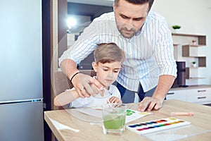 Father and son paint on the paper at the table.