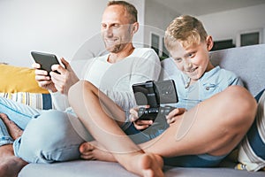 Father and son, PC gamers, enthusiastically playing with electronic devices: tablet and gamepad
