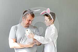 father and son pet a white rabbit on a gray background