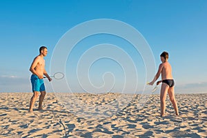 Father and son play badminton on the beach on a sunny day. Outdoor sports family games. Active healthy lifestyle concept