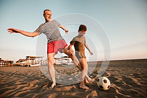 Father and son play football on the beach having great family time on summer holidays