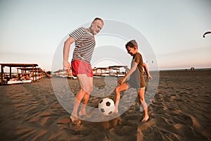 Father and son play football on the beach having great family time on summer holidays