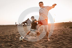 Father and son play football on the beach having great family time on summer holidays