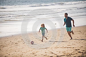 Father and son play soccer or football on the beach on summer family holidays. Dad and child playing outdoor.