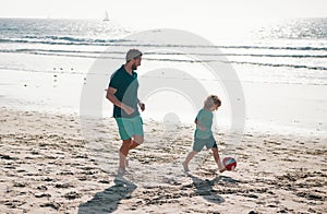 Father and son play soccer or football on the beach on summer family holidays. Dad and child playing outdoor.
