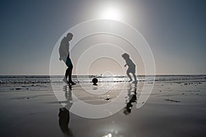 Father and son play soccer or football on the beach on summer family holidays. Daddy with kid boy playing on a summer