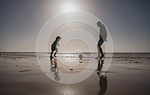 Father and son play soccer or football on the beach on summer family holidays. Daddy with kid boy playing on a summer