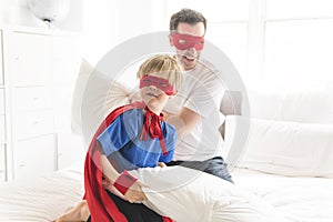 Father and son play superheroes on bed at home