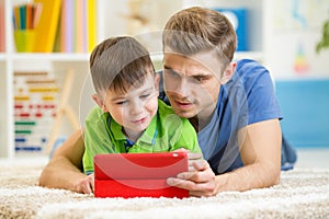 Father and son play with tablet computer at home