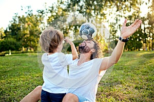 Father son playing with a ball on the grass in the park.