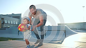 father and son playing ball at the skate park. happy family a kid dream concept. father plays with his baby son with