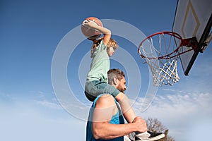 Father and son playing basketball. Happy father holding his little son on shoulders, helping him to score a basket on a